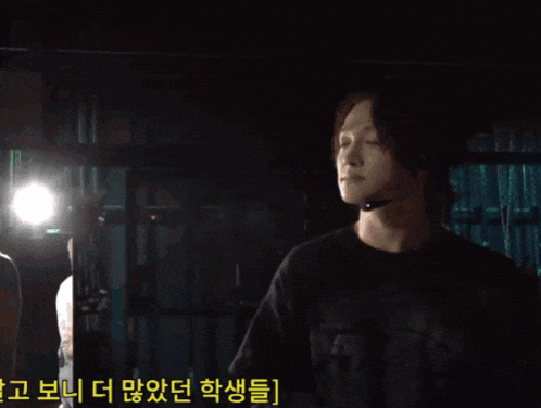 a man holding a bottle of water in a dark room with korean writing on the bottom