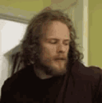 a man with long hair and a beard is standing next to a door .