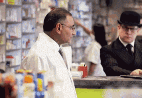 a man in a bowler hat is talking to another man in a pharmacy
