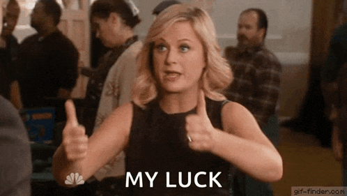 a woman is giving a thumbs up and the words `` my luck '' are visible behind her .