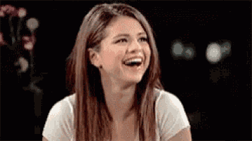 a woman is laughing while wearing a white shirt and looking at the camera .