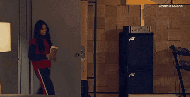 a woman in a red sweater is holding a book in front of a speaker labeled ' fender '