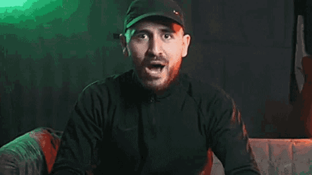 a man with a beard wearing a black hat is screaming in a dark room .