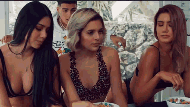a group of women sitting around a bowl of cereal including one wearing a shirt that says " dont tell anyone "