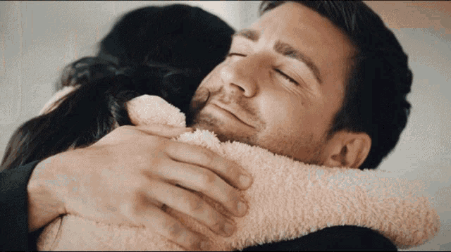 a man is hugging a woman who is wearing a pink sweater