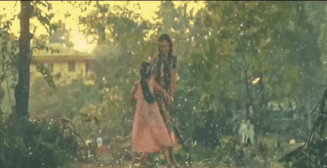 a woman and a little girl are holding hands in the rain in a forest .