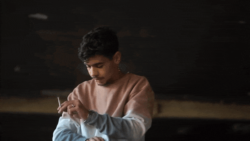 a man in a tie dye sweater is holding a cigarette in his hand