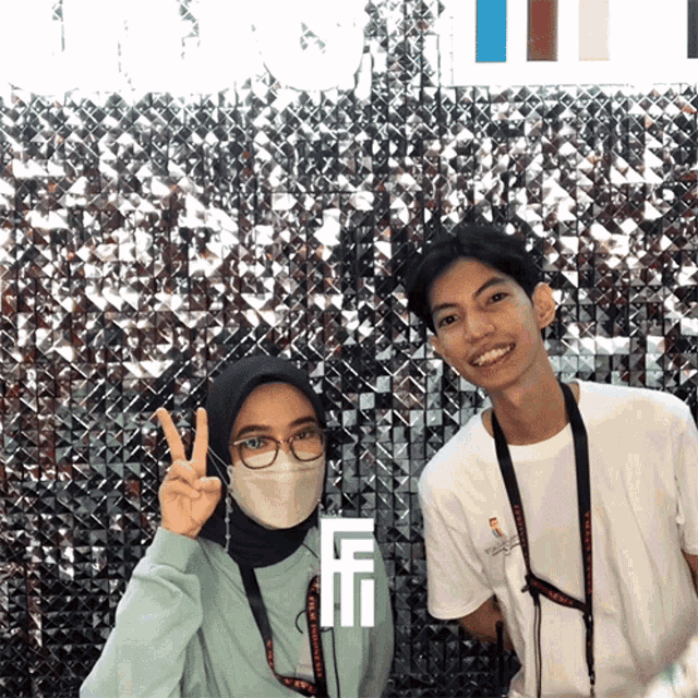 a woman wearing a mask and a man wearing a lanyard with the letter f on it pose for a photo