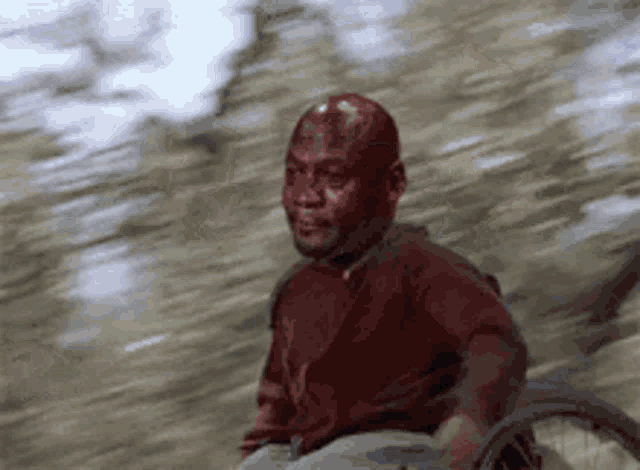a man in a wheelchair with blood on his face is riding down a road .