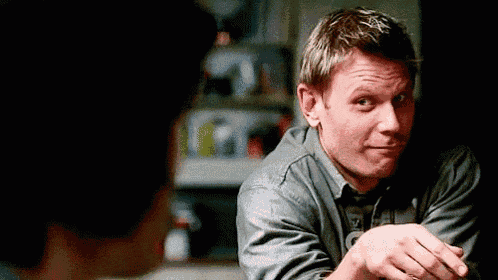 a man is sitting at a table with his hands folded in front of a woman and making a face .