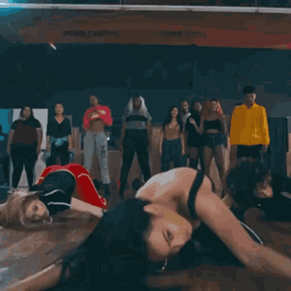 a group of people are dancing in a dance studio and one woman is wearing a red crop top that says supreme