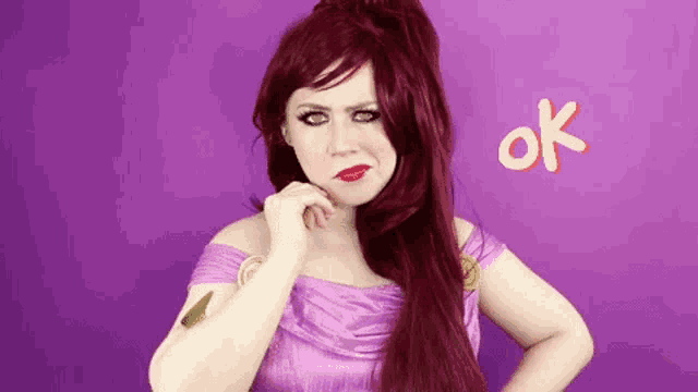 a woman with red hair is wearing a purple dress and making an ok sign with her hand on her chin .