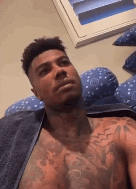 a shirtless man with tattoos on his chest is laying on a bed with a towel around his neck .