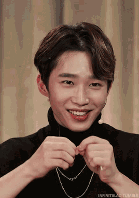 a young man wearing a black turtleneck and a necklace is smiling for the camera