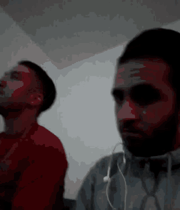 two men are sitting next to each other in a dark room . one of the men is wearing headphones .