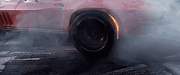 a red car is doing a burnout on the road and smoke is coming out of the tire .