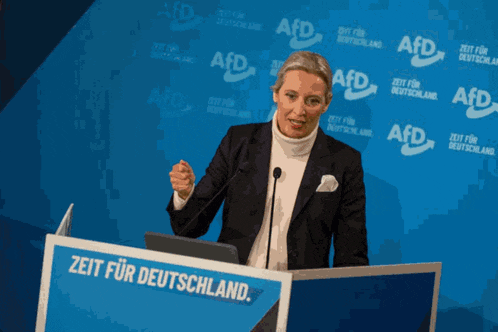 a woman stands at a podium that says zeit für deutschland