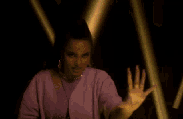 a woman in a purple jacket is dancing in a dark room with a spotlight shining on her hand .