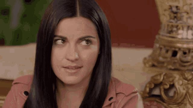 a woman with long black hair is wearing a pink jacket and making a funny face