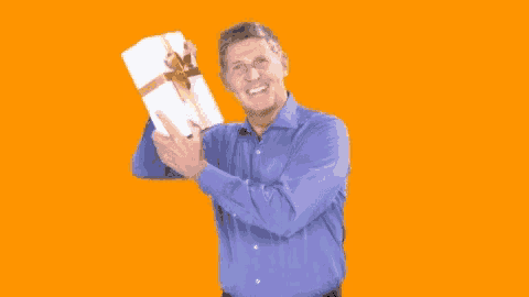 a man in a blue shirt is holding a white box with a gold bow