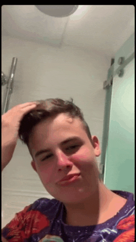 a young man in a purple shirt is looking at his hair