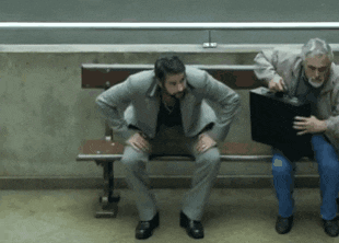 a man in a suit sits on a bench while another man holds a black briefcase