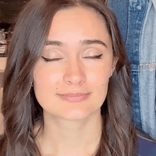 a woman with her eyes closed is wearing earrings and a denim jacket .