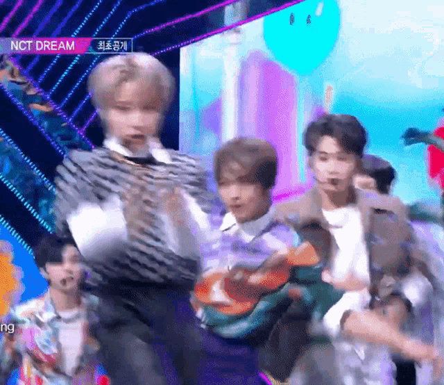 a group of young men are dancing on a stage with nct dream in the background .