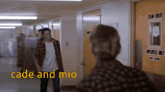 a man in a plaid shirt is talking to another man in a hallway with the words cade and mio written on it