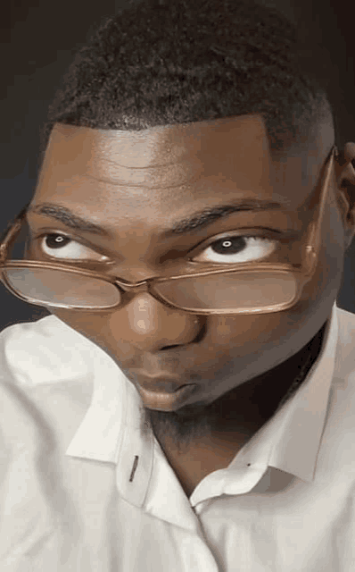 a young man wearing glasses and a white shirt looks at the camera