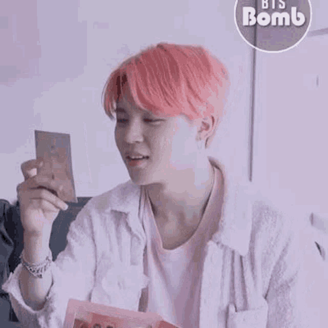 a young man with pink hair is holding a picture of himself in his hand .