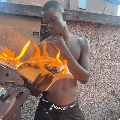 a shirtless man wearing nike shorts is holding a piece of paper on fire