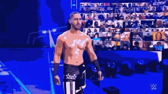 a shirtless wrestler stands in front of a crowd with a w logo on his chest