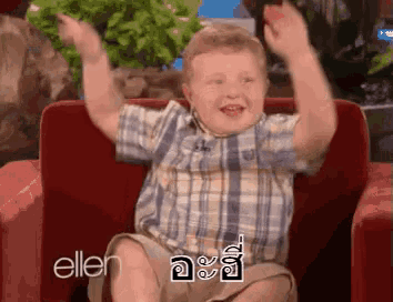 a young boy is sitting in a red chair with his arms in the air .