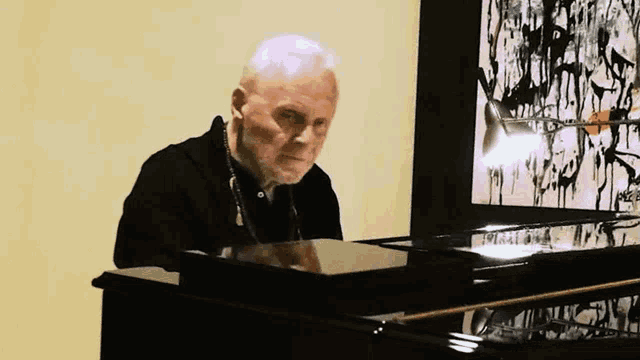 a man is playing a piano in front of a painting