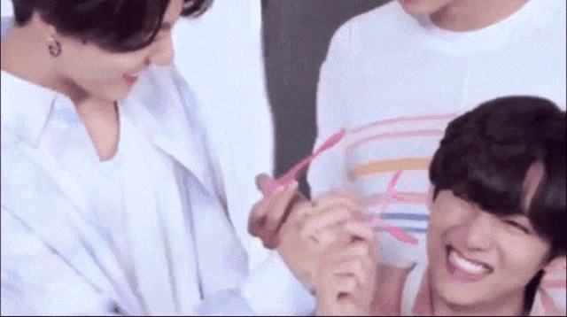 a group of young men are holding hands and smiling while one of them is holding a pink toothbrush .