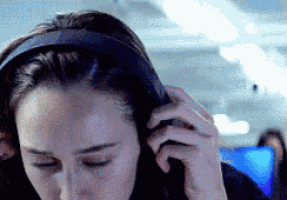 a woman wearing headphones on an airplane looks down at something
