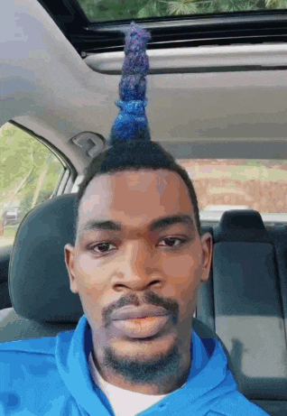 a man in a blue hoodie is sitting in the driver 's seat of a car with his hair in a mohawk .
