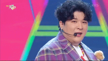 a man in a purple plaid jacket is holding a teddy bear and wearing a microphone on his head .