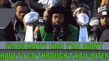 a man in a green jacket holds a super bowl trophy in front of a crowd of people