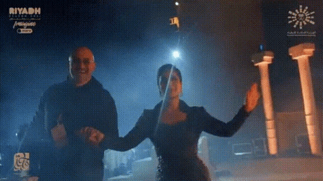 a man and a woman are dancing in front of a sign that says riyadh on it