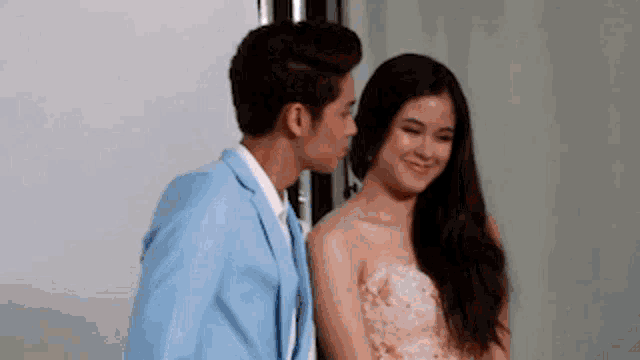 a man in a blue jacket kisses a woman in a pink dress