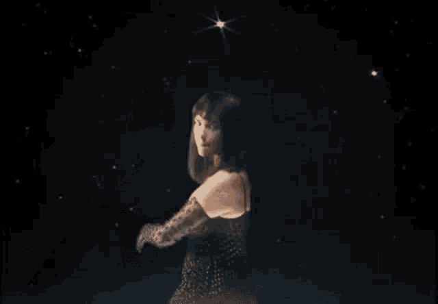 a woman in a black dress is standing in a dark room holding her arm up .