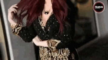 a woman with long red hair is wearing a black and gold dress and holding her hair .