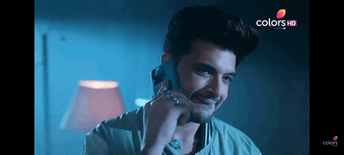 a man is smiling while talking on a cell phone with a colors hd logo in the background
