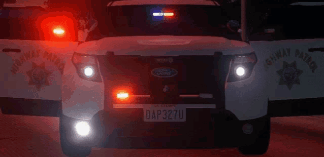 two highway patrol vehicles are parked next to each other with their doors open at night .