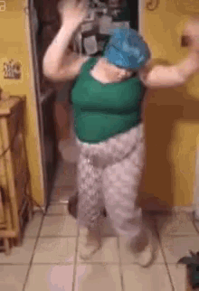 a woman in a green tank top and pink pants is dancing on a tiled floor .
