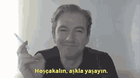 a man smoking a cigarette with a caption that says hoscakalin aşkla yasayin