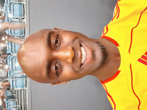 a man wearing a yellow shirt with red stripes on the sleeves is smiling