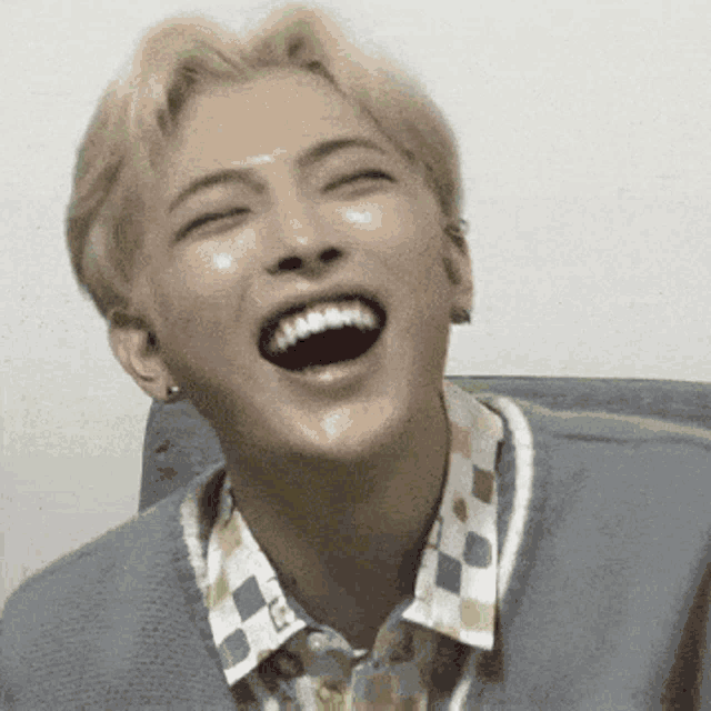a young man is laughing with his mouth open while sitting on a couch .